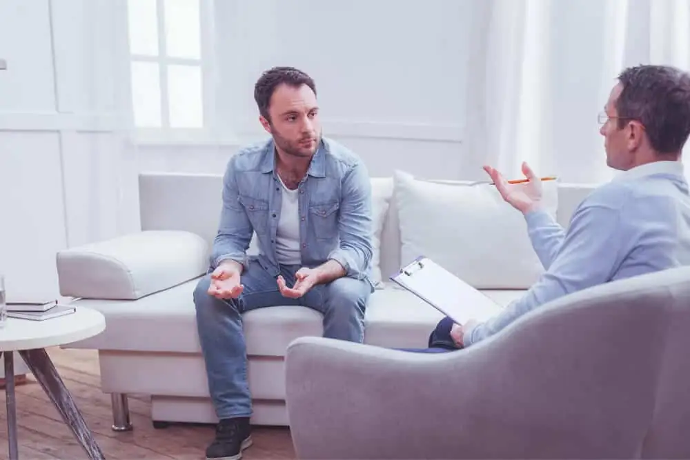 Two men sitting on couches in a clinic, engaged in conversation during a therapy session.